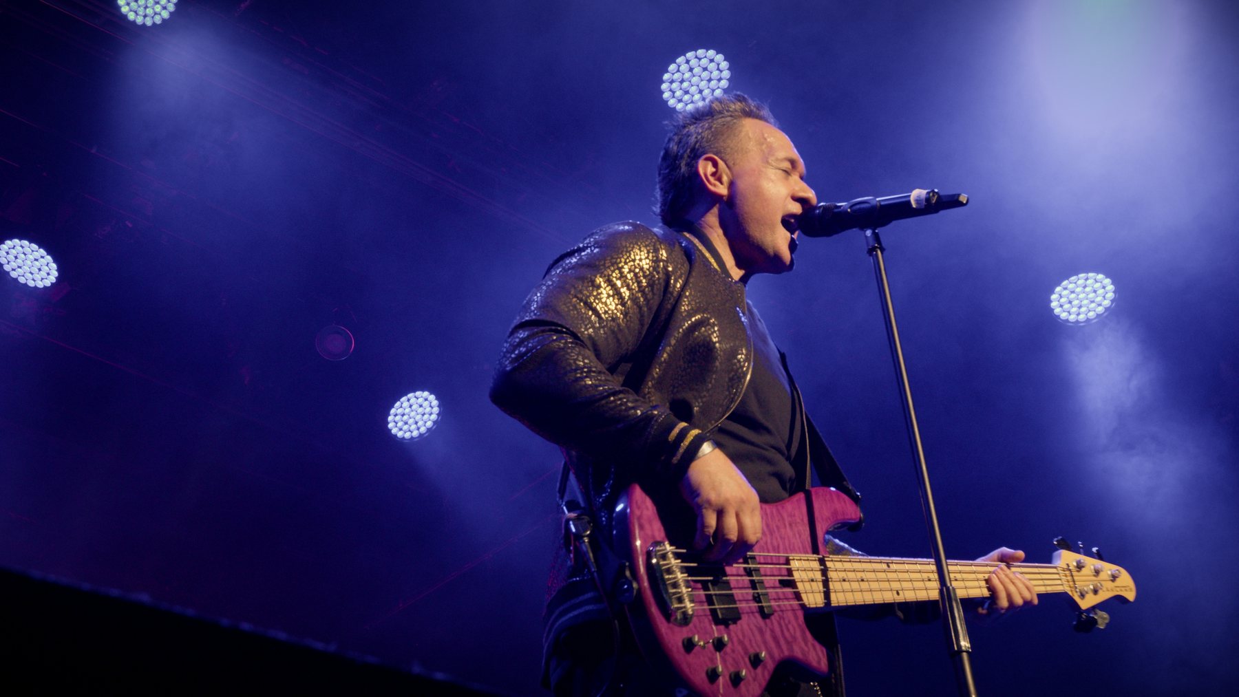 A bassist singing into a mic under blue stage lights